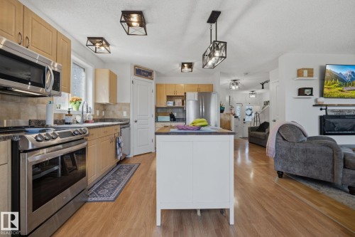 Kitchen featuring stainless steel appliances, light wood cabinetry, stone-finish countertops, and wood-finish flooring - 60 Leyland Way, Spruce Grove, AB 