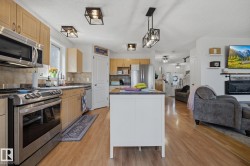 Kitchen featuring stainless steel appliances, light wood cabinetry, stone-finish countertops, and wood-finish flooring - 