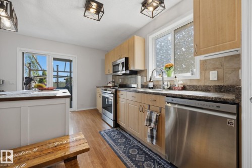 Kitchen featuring light wood-finish cabinetry, stainless steel appliances, dark stone-finish countertops, and a tile backsplash - 60 Leyland Way, Spruce Grove, AB 
