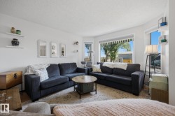 Bright living area featuring a large bay window, wall-mounted floating shelves, and an area rug over wood-finish flooring - 