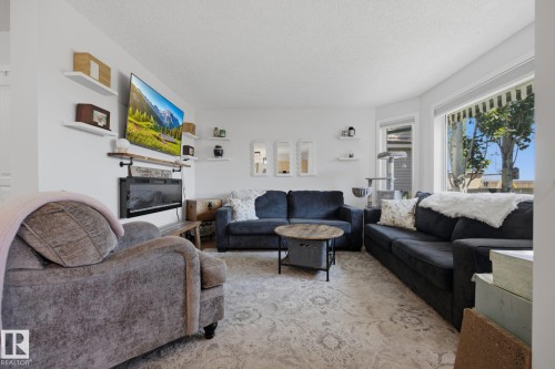 Living area featuring an electric fireplace with a wood mantle, white floating shelves, and bay windows - 60 Leyland Way, Spruce Grove, AB 