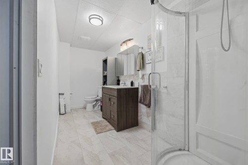 Bathroom featuring a rounded glass-enclosed shower, wood-finish vanity with countertop sink, and light-toned tile flooring - 60 Leyland Way, Spruce Grove, AB 