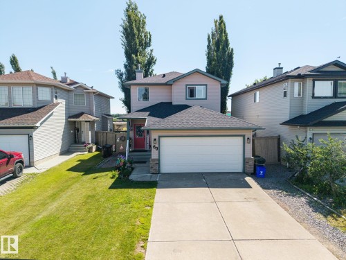 Two-story residential property featuring a light-colored exterior with dark trim accents, an attached two-car garage with a white door, a red front entry door, and a paved driveway - 60 Leyland Way, Spruce Grove, AB 