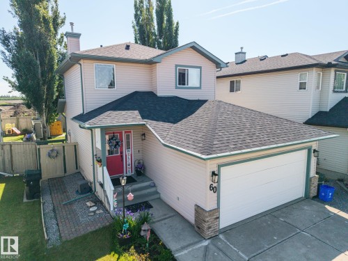 Two-story residence featuring light-colored siding, a dark shingle roof, and a prominent red front door - 60 Leyland Way, Spruce Grove, AB 