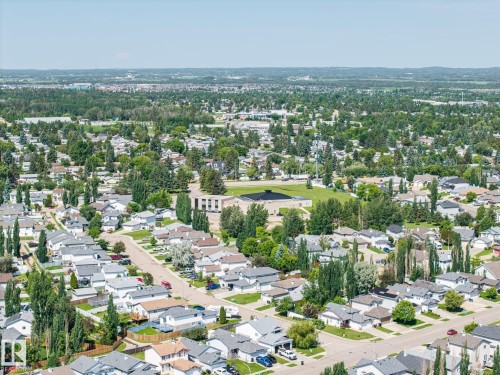 Expansive aerial view showcasing residential streets with numerous single-family homes, mature trees, and a central community building with a large open field - 60 Leyland Way, Spruce Grove, AB 