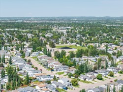 Expansive aerial view showcasing residential streets with numerous single-family homes, mature trees, and a central community building with a large open field - 