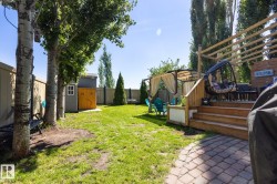 Expansive backyard featuring a multi-level wooden deck with pergola, brick paver patio, manicured lawn, and two storage sheds - 