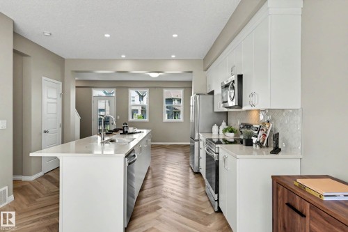 Modern kitchen featuring white cabinetry, stainless steel appliances, and a central island with a sink - 53 2072 Wonnacott Way, Edmonton, AB 