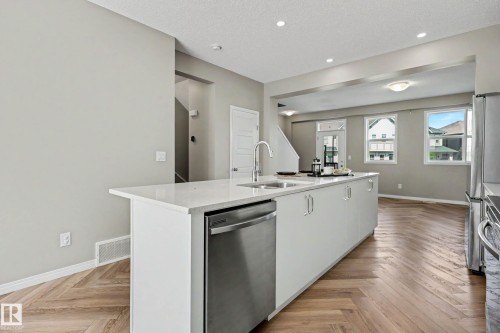 Kitchen island featuring a stainless steel dishwasher, an undermount sink with a gooseneck faucet, and a light-toned countertop - 53 2072 Wonnacott Way, Edmonton, AB 