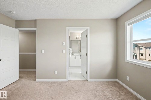 Neutral-toned bedroom featuring carpet flooring, a spacious open closet, and a white framed window - 53 2072 Wonnacott Way, Edmonton, AB 