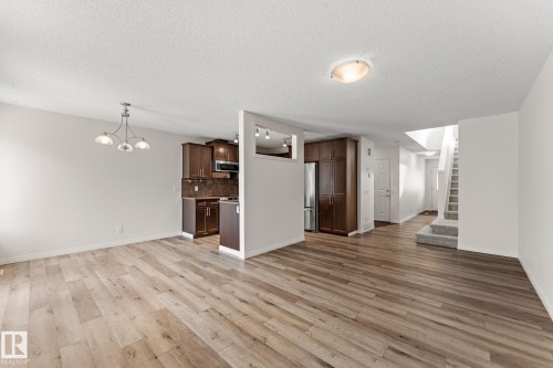 Open-concept living area featuring wood-finish flooring, white walls, and a contemporary chandelier - 12523 171 Avenue, Edmonton, AB 