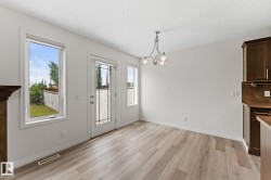 Spacious dining area featuring wood-finish flooring, ample natural light from multiple windows, a glass-paned door, a contemporary chandelier, and rich wood cabinetry with a coordinating backsplash - 