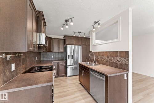 Kitchen featuring wood-finish cabinetry, stainless steel appliances, a tile backsplash, light wood-finish flooring, and track lighting - 12523 171 Avenue, Edmonton, AB 