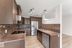 Kitchen featuring wood-finish cabinetry, stainless steel appliances, a tile backsplash, light wood-finish flooring, and track lighting - 