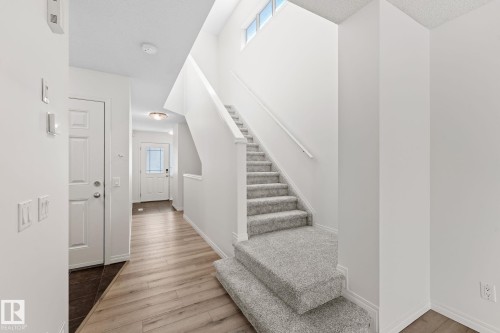 Foyer featuring a light wood-finish flooring, a white paneled door, and a staircase with light grey carpeting and a handrail - 12523 171 Avenue, Edmonton, AB 