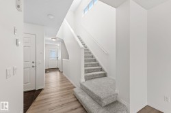 Foyer featuring a light wood-finish flooring, a white paneled door, and a staircase with light grey carpeting and a handrail - 