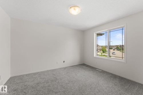 Bright interior space featuring a large window with multiple panes, gray carpet flooring, white walls, and a ceiling light fixture - 12523 171 Avenue, Edmonton, AB 