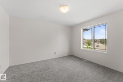 Bright interior space featuring a large window with multiple panes, gray carpet flooring, white walls, and a ceiling light fixture - 