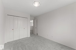 Bedroom featuring light gray carpeting, white walls, a flush-mount ceiling light fixture, and bifold closet doors with round wooden knobs - 