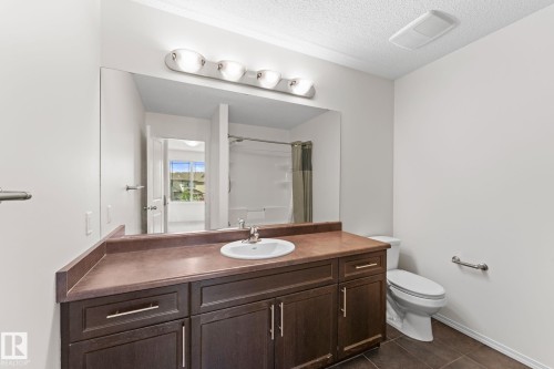 Bathroom featuring a dark wood-finish vanity with a single basin sink, large wall-mounted mirror, and overhead lighting fixture - 12523 171 Avenue, Edmonton, AB 