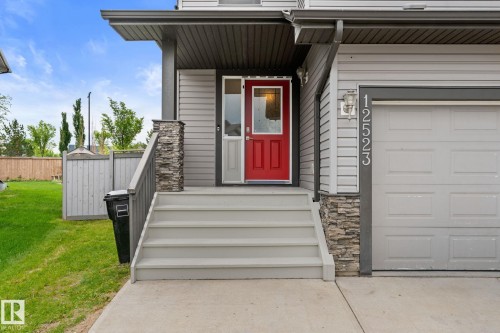 Front entry featuring a vibrant red door, covered porch, concrete steps, and a garage with vertical house numbers - 12523 171 Avenue, Edmonton, AB 