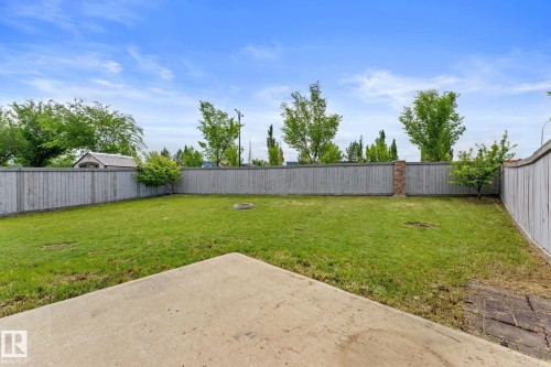 Expansive backyard featuring a large concrete patio, lush green lawn, full perimeter wood fencing, and mature trees - 12523 171 Avenue, Edmonton, AB 