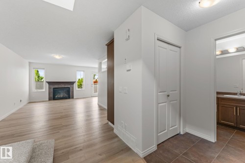 Open-concept living area with light wood-finish flooring, a contemporary fireplace with a dark mantel, and multiple windows providing natural illumination - 12523 171 Avenue, Edmonton, AB 