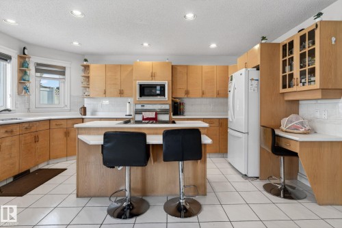 Kitchen featuring wood cabinetry, white tile flooring, white countertops, built-in microwave, and a central island with breakfast bar seating - 4615 43A Avenue, Edmonton, AB - Indoor Photo Showing Kitchen