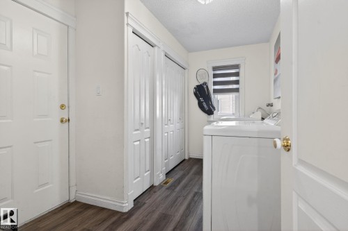 Dedicated laundry area featuring wood-finish flooring, a white paneled door with brass hardware, and built-in bifold closet doors - 4615 43A Avenue, Edmonton, AB - Indoor Photo Showing Laundry Room