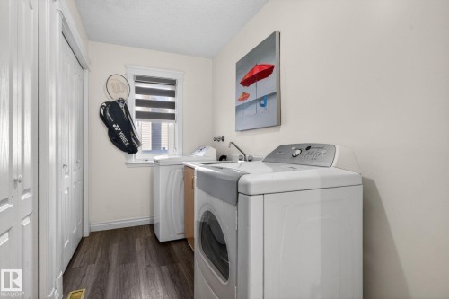 Dedicated laundry room featuring dark wood-finish flooring, white bifold closet doors, a single window with horizontal blinds, and a utility sink - 4615 43A Avenue, Edmonton, AB - Indoor Photo Showing Laundry Room