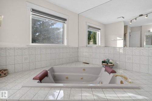 Corner jetted tub set within a tiled surround featuring two windows and a mirrored wall - 4615 43A Avenue, Edmonton, AB - Indoor Photo Showing Bathroom