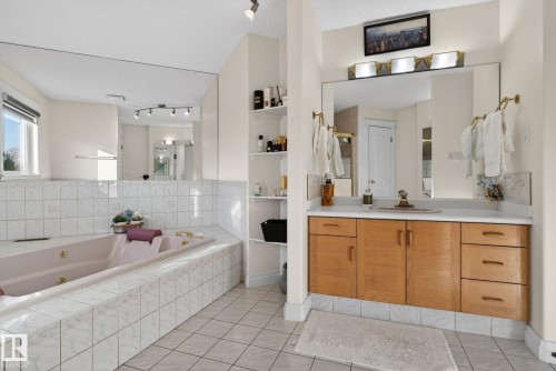 Bathroom featuring a built-in jetted tub surrounded by white tiled walls, a wood-finish vanity with a single sink, an expansive wall-mounted mirror, and recessed shelving - 4615 43A Avenue, Edmonton, AB - Indoor Photo Showing Bathroom