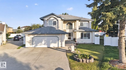 Stucco exterior residence featuring a two-car attached garage, arched window accents, a front lawn with established landscaping, and a side yard with white fencing - 4615 43A Avenue, Edmonton, AB - Outdoor