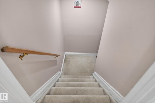 Carpeted staircase with light-toned wall paint, white trim, and a wood handrail with brass-toned brackets - 4615 43A Avenue, Edmonton, AB - Indoor Photo Showing Other Room