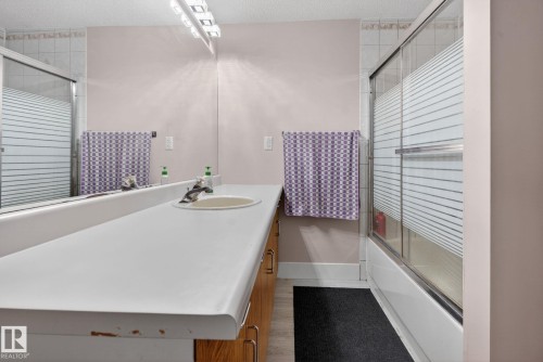 Bathroom featuring a spacious vanity with an integrated sink, extended countertop, wood-finish cabinetry, and a full-width mirror - 4615 43A Avenue, Edmonton, AB - Indoor Photo Showing Bathroom