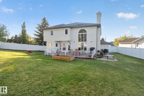 Expansive rear yard featuring a manicured lawn, a white privacy fence, a raised deck with white railings, and a large arched window on the rear elevation - 4615 43A Avenue, Edmonton, AB - Outdoor