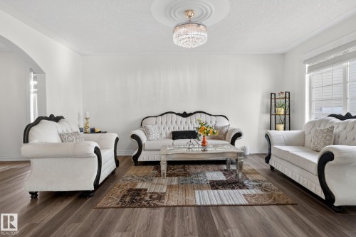 Spacious living area featuring wood-finish flooring, white painted walls, crown molding, and an elegant crystal chandelier with a ceiling medallion - 4615 43A Avenue, Edmonton, AB - Indoor Photo Showing Living Room