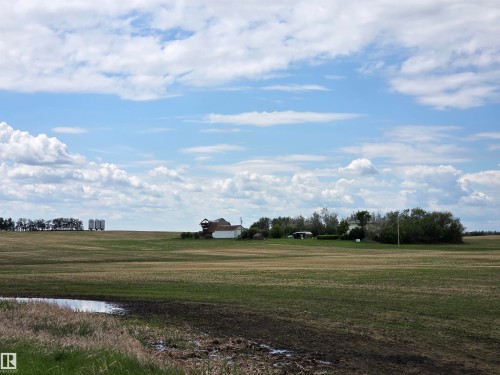 Expansive agricultural land featuring a distant farmstead, multiple grain silos, and mature trees - 24209 Hwy 625, Beaumont, AB 
