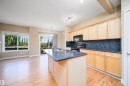 Kitchen featuring a central island with a sink, wood-finish flooring, light wood cabinetry, dark speckled countertops, and a black appliance suite - 46 15151 43 Street, Edmonton, AB 