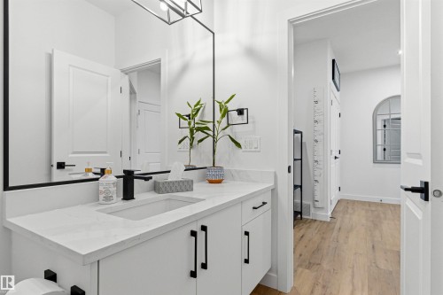 Bathroom featuring a single vanity with a light-colored countertop and integrated sink, black matte faucet, and white cabinetry with black hardware - 7 Tenor Link, Spruce Grove, AB 