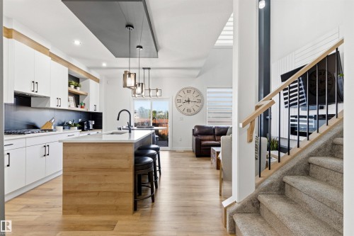 Open-concept kitchen featuring white cabinetry, wood-finish flooring, a central island with a waterfall countertop, and pendant lighting - 7 Tenor Link, Spruce Grove, AB 