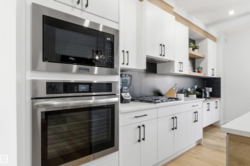 Kitchen featuring stainless steel built-in microwave and oven, a gas cooktop, white cabinetry with black hardware, and an expansive countertop - 7 Tenor Link, Spruce Grove, AB 