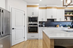 Modern kitchen featuring white cabinetry, light wood-finish flooring, a stainless steel refrigerator, built-in microwave and oven, and a kitchen island with a light-toned countertop - 