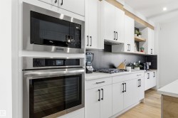 Kitchen featuring stainless steel built-in microwave and oven, a gas cooktop, white cabinetry with black hardware, and an expansive countertop - 