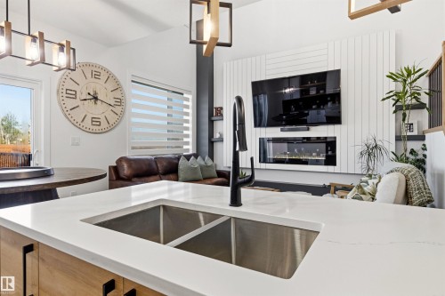 Kitchen island featuring a double basin stainless steel sink, black gooseneck faucet, and light-toned wood-finish cabinetry with black hardware - 7 Tenor Link, Spruce Grove, AB 