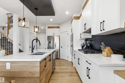 Modern kitchen featuring light wood-finish flooring and an island with a built-in sink and matte black faucet - 7 Tenor Link, Spruce Grove, AB 