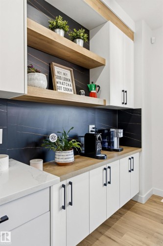 Modern kitchen area featuring white cabinetry with matte black hardware, wood-finish countertops, and an accent backsplash - 7 Tenor Link, Spruce Grove, AB 