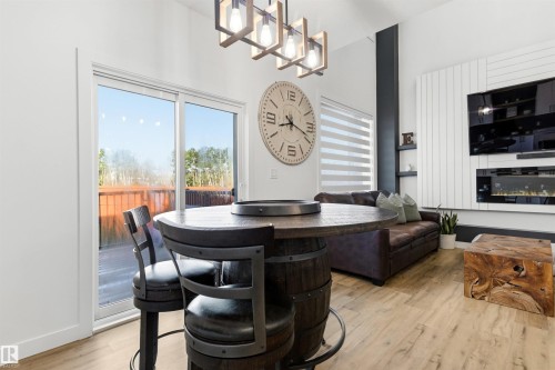 Spacious living area featuring wood-finish flooring, a contemporary ceiling fixture, a built-in electric fireplace, and a sliding glass door opening to an outdoor deck - 7 Tenor Link, Spruce Grove, AB 