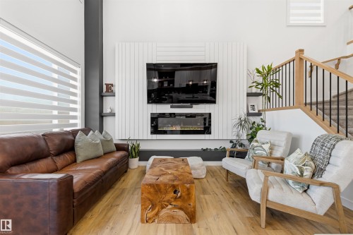 Spacious living area featuring light wood-finish flooring, a contemporary fireplace with shiplap-style surround, built-in shelving, and a natural wood staircase with black metal balusters - 7 Tenor Link, Spruce Grove, AB 