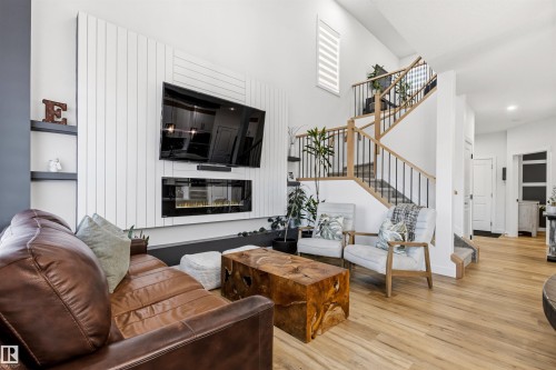 Living area featuring a vertical slat accent wall with an integrated linear fireplace, built-in shelving, and light wood-finish flooring - 7 Tenor Link, Spruce Grove, AB 